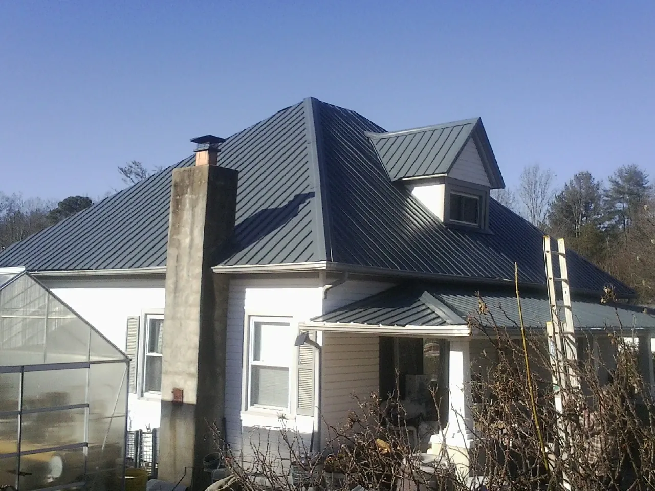 Dark blue standing seam metal roof on a white farmhouse with dormer — Slate & Tile Roof Repair by Roofing Brothers in Philpot