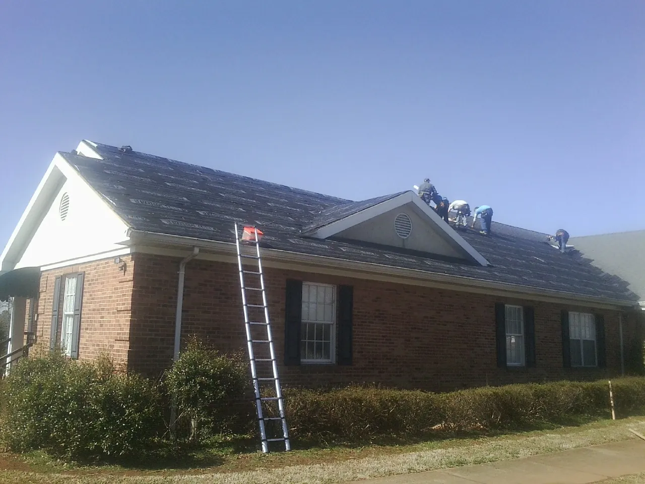Crew tearing shingles off a brick ranch roof with a ladder set — Metal Roof Repair work by our crew in Philpot