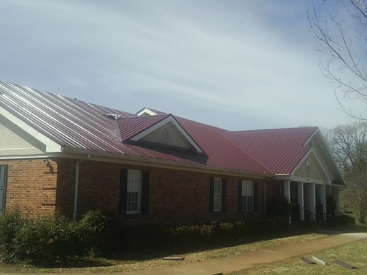 Red metal roof with gabled entries on a long brick building, from a Hail Damage Roof Repair job in Philpot