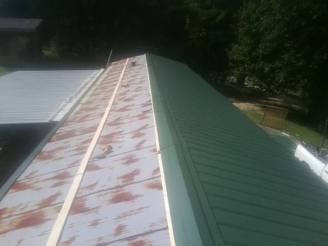 Old rusted panels beside newly installed green metal roofing — Wind Damage Roof Repair by Roofing Brothers in Philpot
