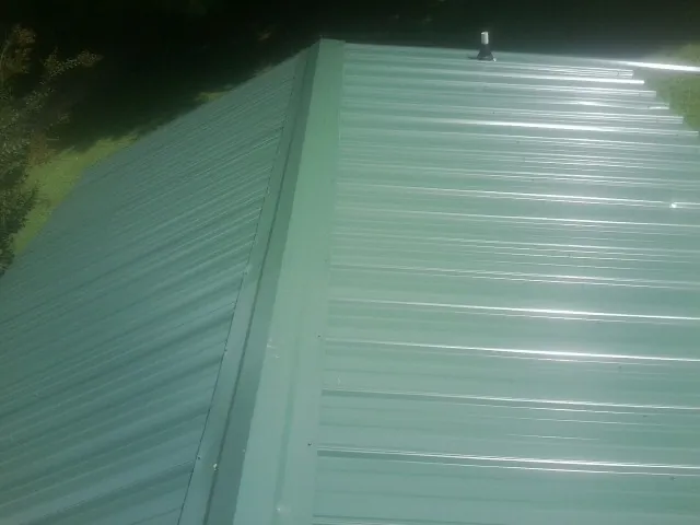 New green metal panels meeting at the ridge of a roof — Flat Roof Repair work by our crew in Philpot