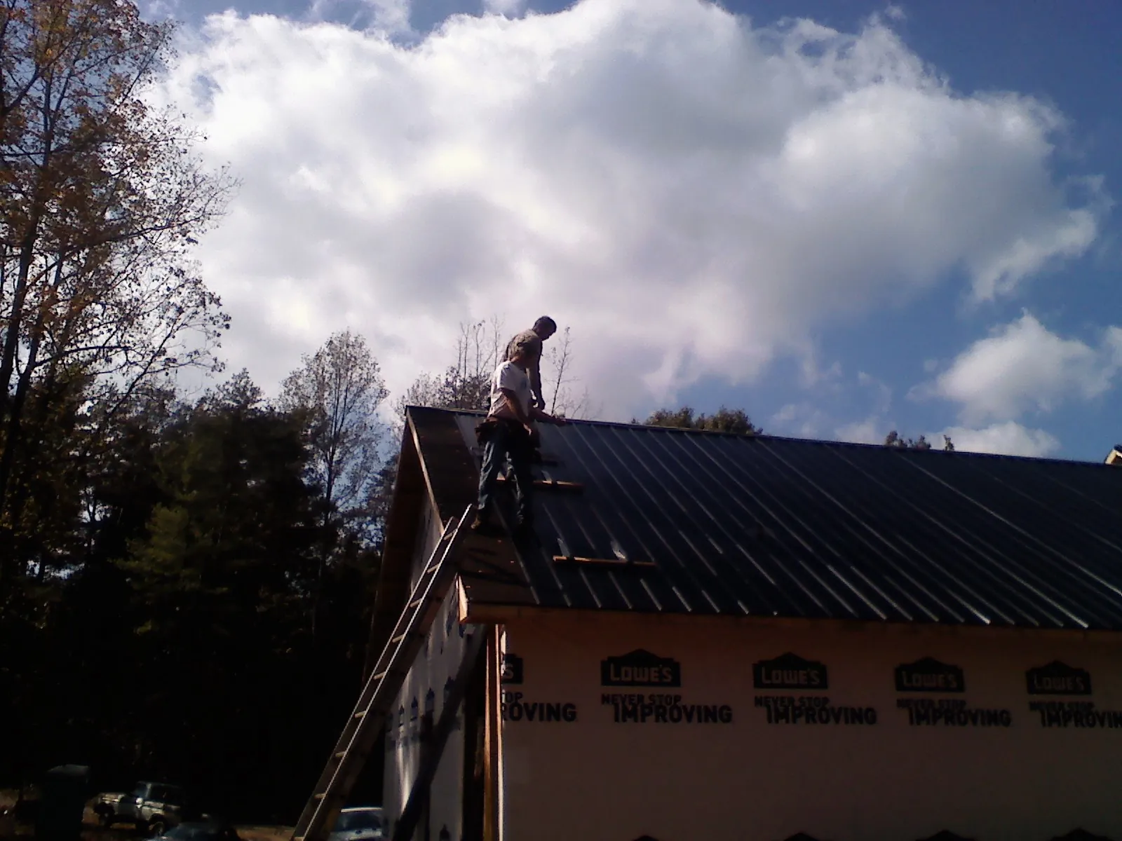Roofer fastening dark metal panels high against a cloudy sky, from a Roof Inspection job in Philpot