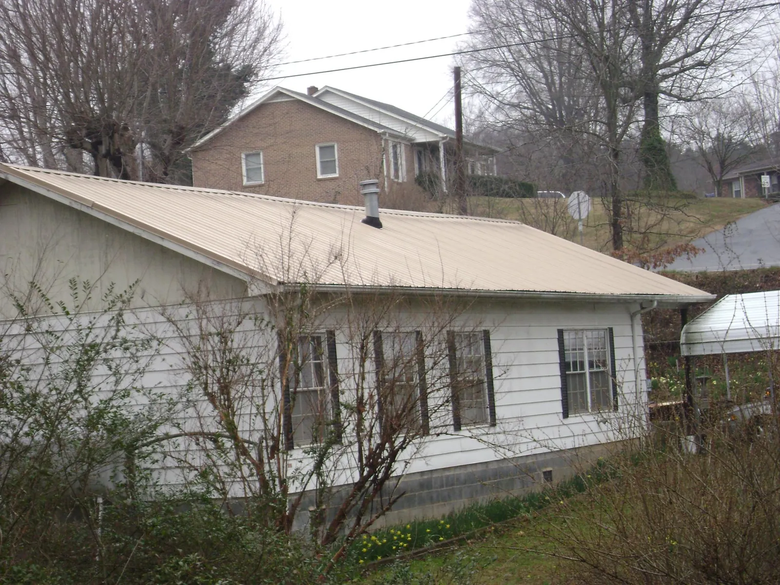 Tan metal roof on a white sided house set into a hillside — Commercial Roofing by Roofing Brothers in Philpot